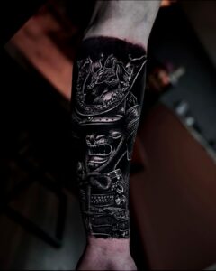 Zwart-grijze onderarmtattoo van een gedetailleerde samoeraihelm met draak, in realistische stijl