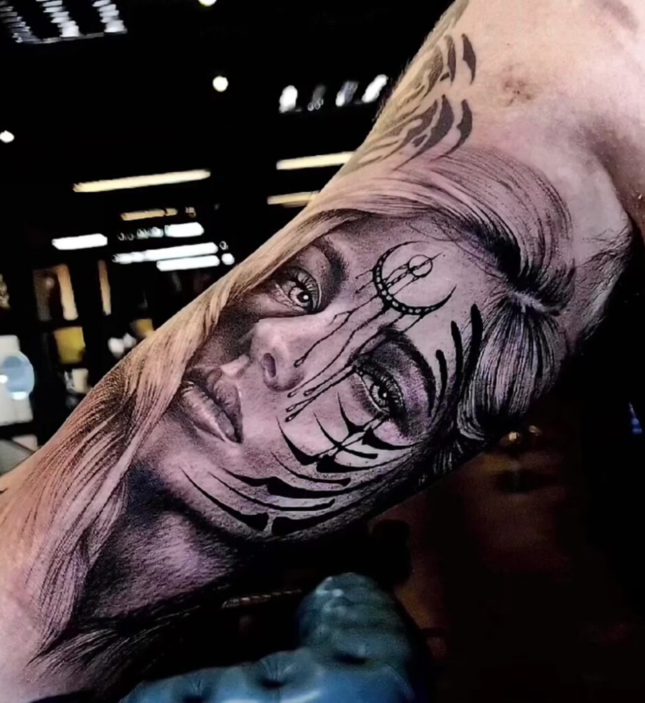 Tattoo van een vrouwengezicht met symbolische tribal-achtige markeringen, realistisch gezet op de onderarm