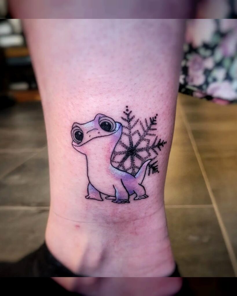 Kleine tattoo van Bruni, het salamandertje uit Disney's Frozen 2, met een sierlijke sneeuwvlok op de achtergrond op het onderbeen