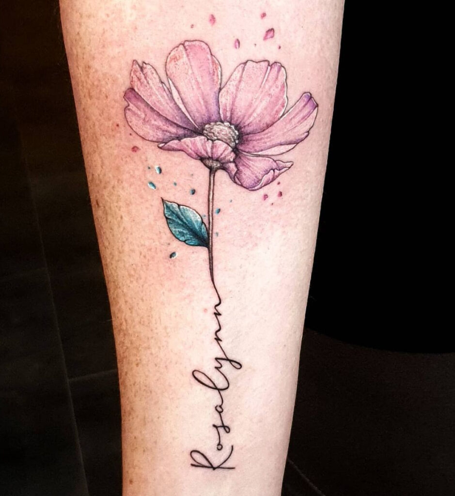 Tattoo van roze bloem met blauw blad en de naam Rosalyn als steel, gezet op het been bij Tat2holics in Den Haag