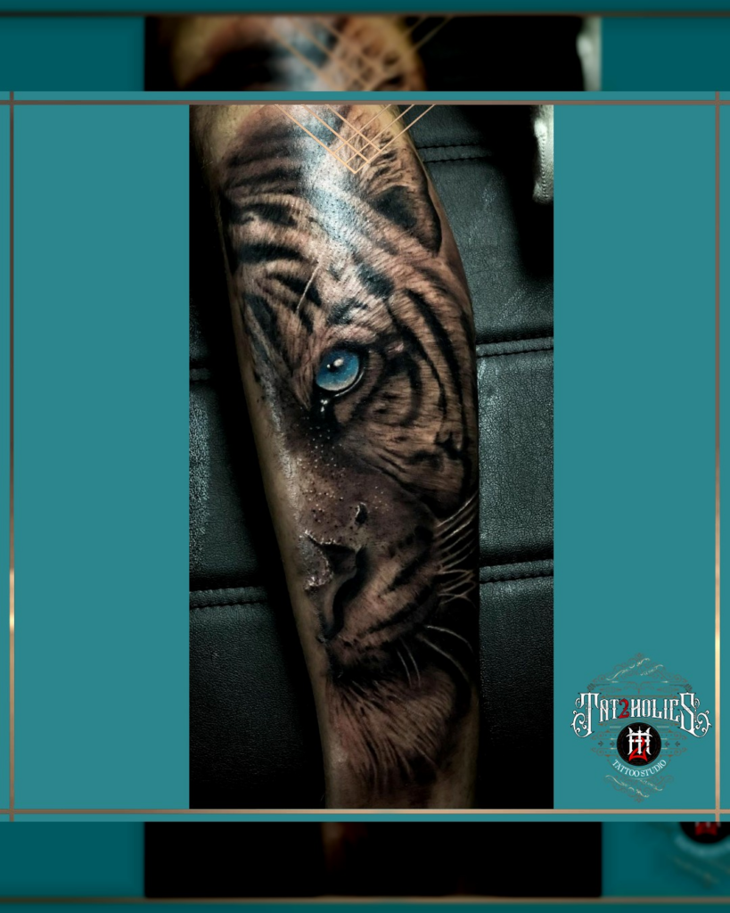 Tattoo van een tijgerkop met intens blauwe ogen, realistisch gezet op het onderbeen