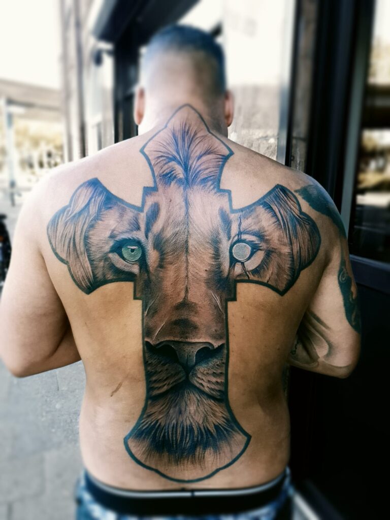 Tattoo van een realistische leeuwenkop in kruisvorm, geplaatst op de volledige rug van een man
