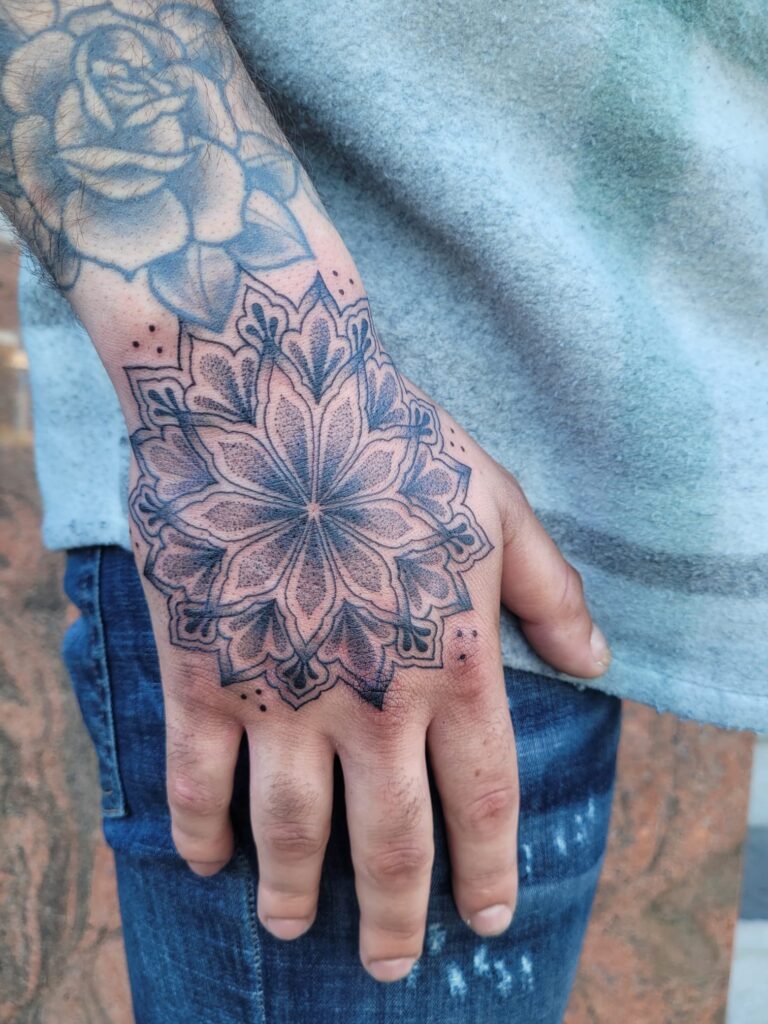 Gedetailleerde mandala tattoo op de bovenkant van de hand met dotwork schaduwwerking en strakke lijnstijl, gezet bij Tat2holics in Den Haag
