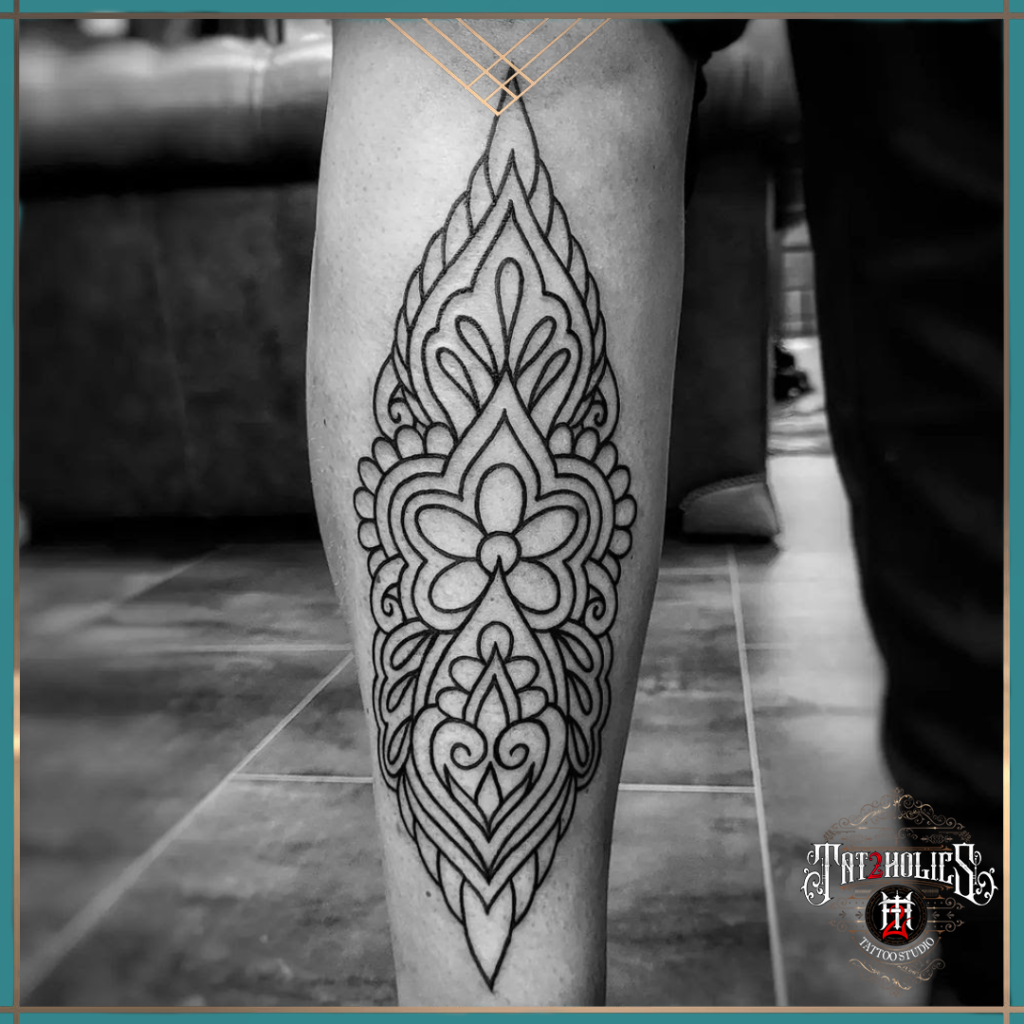 Zwarte fineline tattoo op het onderbeen, met symmetrisch sierpatroon geïnspireerd op mandala en ornamentale vormen