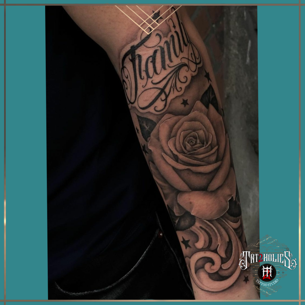 Tattoo met sierlijke naam in script lettering en grote roos op de onderarm