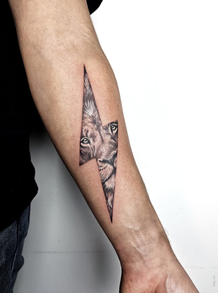 Tattoo van leeuwengezicht in realistische stijl verwerkt in een bliksemschicht op de onderarm