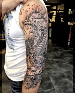 Volledige armtattoo van een Japanse draak in zwart-grijs stijl, met dynamische schubben en intense expressie