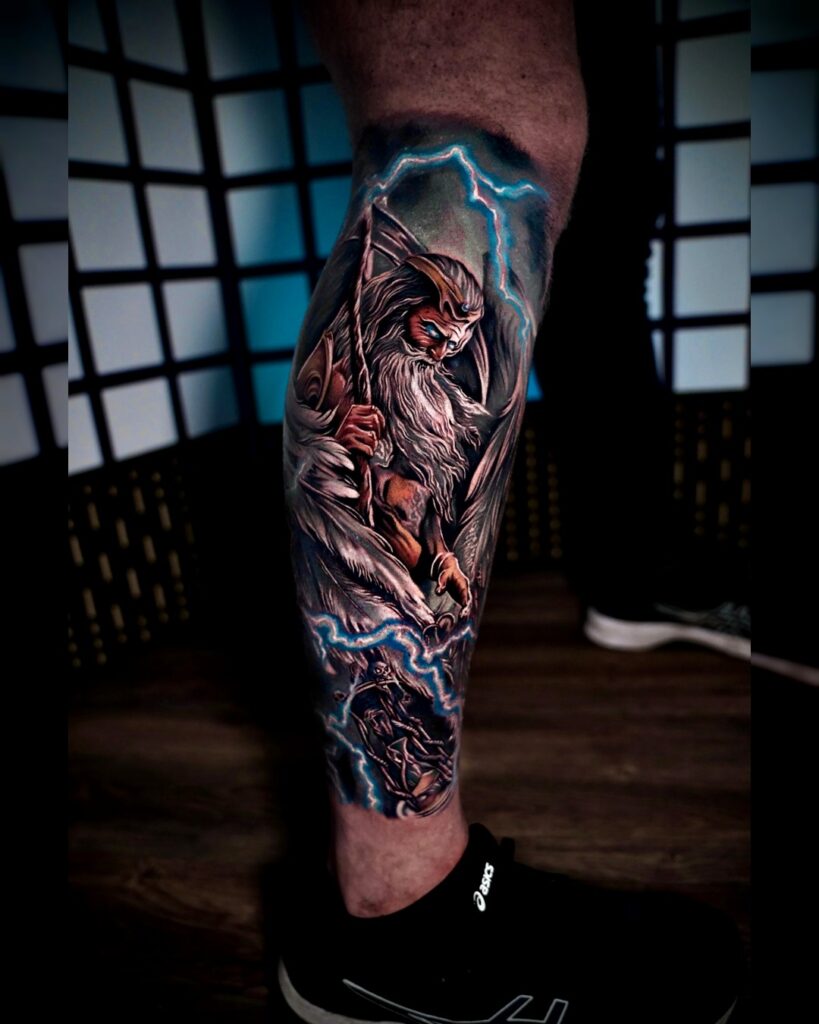 Kleurrijke leg tattoo met gevleugelde krijger met staf, omringd door blauwe bliksemflitsen, gezet bij Tat2holics in Den Haag