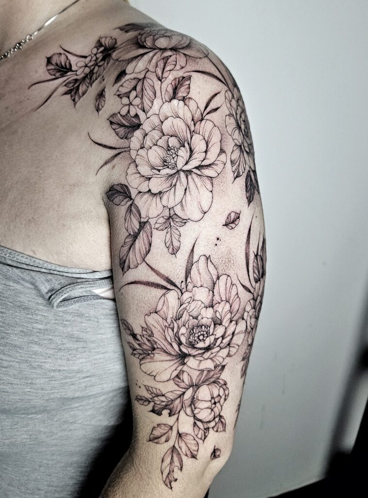 Gedetailleerde bloemen tattoo op bovenarm en schouder, professioneel gezet bij Tat2holics in Den Haag