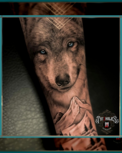 Realistische tattoo van een wolf met blauwe ogen, gecombineerd met een berglandschap op de onderarm