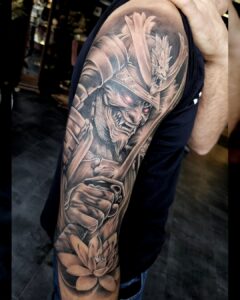 Gedetailleerde tattoo van een demonische samoerai met roodgloeiende ogen en lotusbloem op de onderarm