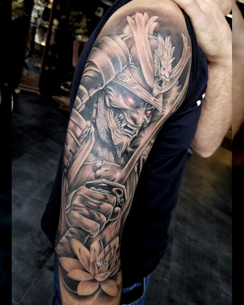 Gedetailleerde tattoo van een demonische samoerai met roodgloeiende ogen en lotusbloem op de onderarm