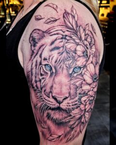 Tattoo van een witte tijger met blauwe ogen, versmolten met bloemen op de schouder