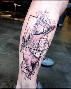 Tattoo van een hand met houtschaaf en geometrische lijnen, realistisch en abstract gecombineerd op de kuit