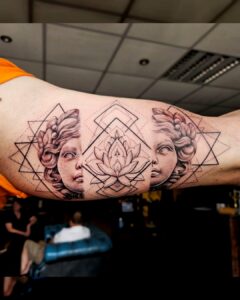 Tattoo op de binnenkant van de bovenarm met twee klassieke vrouwengezichten, geometrische lijnen en een centrale lotusbloem