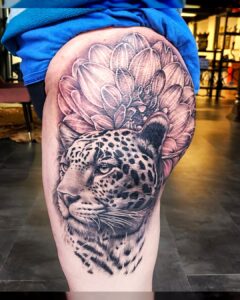 Tattoo van een luipaard gecombineerd met een mandala-achtige bloem, gezet op het bovenbeen